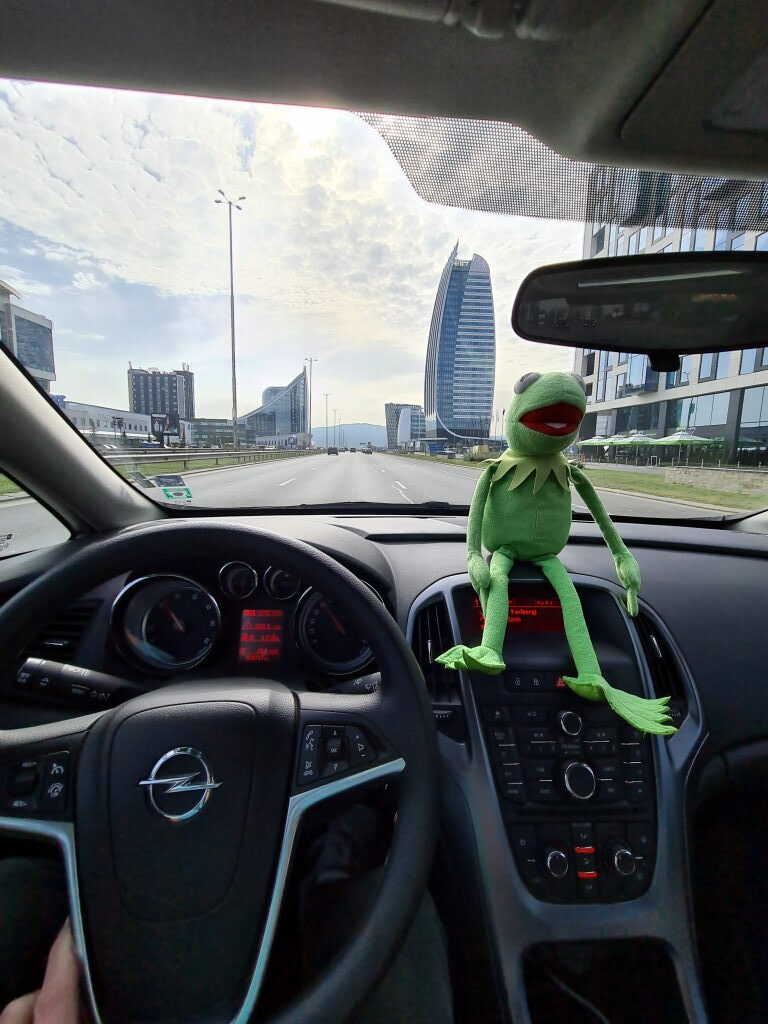 Kermit der Frosch sitzt auf dem Armaturenbrett eines Opel Mietwagens, im Hintergrund die Skyline von Sofia mit modernen Hochhäusern