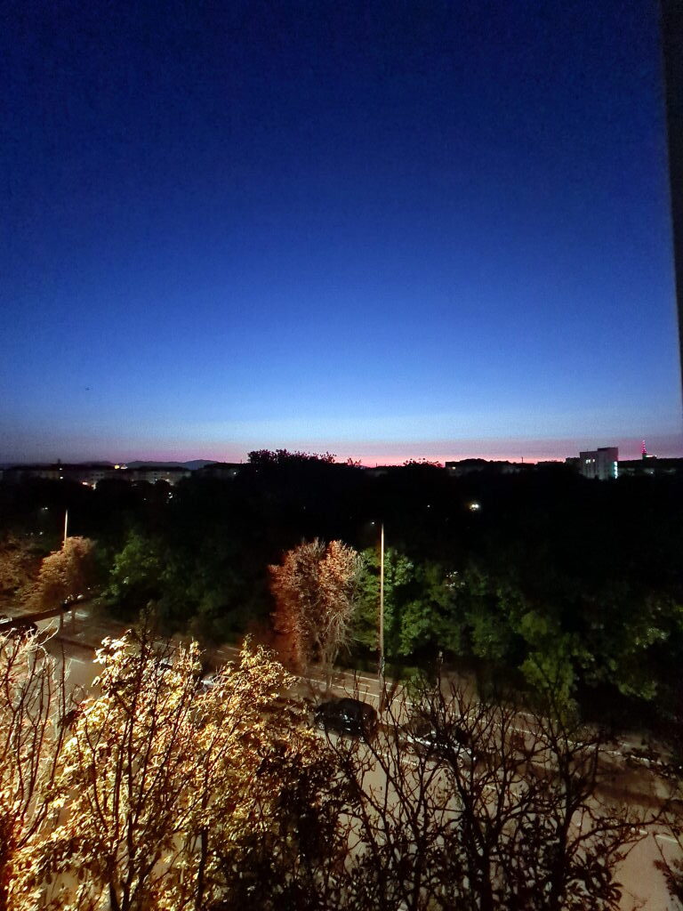 Sonnenaufgang über Sofia mit blauem Himmel und rosa Horizont, Baumkronen im Vordergrund, Fernsehturm rechts