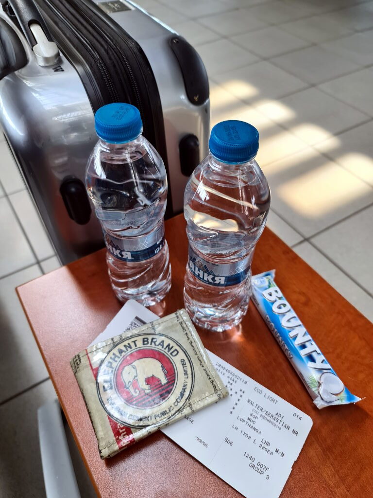 Reisegepäck am Flughafen Sofia mit zwei Flaschen Banka Mineralwasser, einem Bounty-Riegel, einer Bordkarte der Lufthansa und einem Elephant Brand Souvenir
