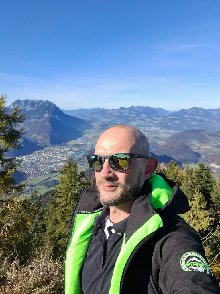 Sebastian mit Sonnenbrille und grüner Weste, Selfie am Pendling-Gipfel mit Panorama