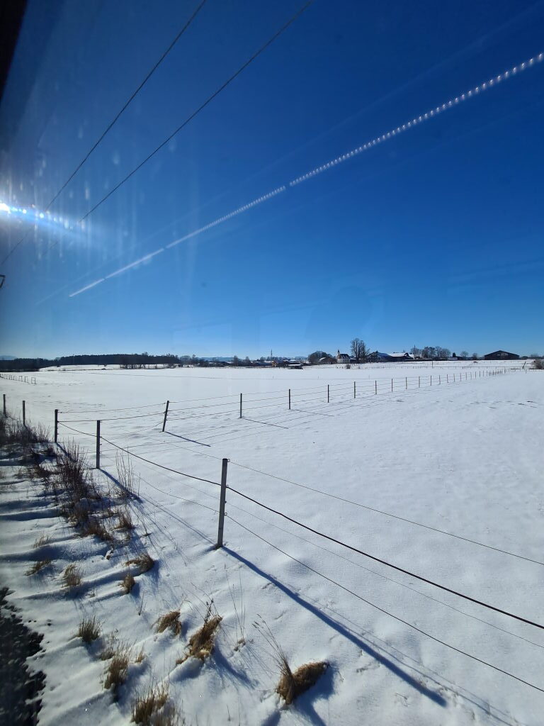 Blick aus dem Zugfenster auf verschneite Felder und Tegernsee im Winter Januar 2022