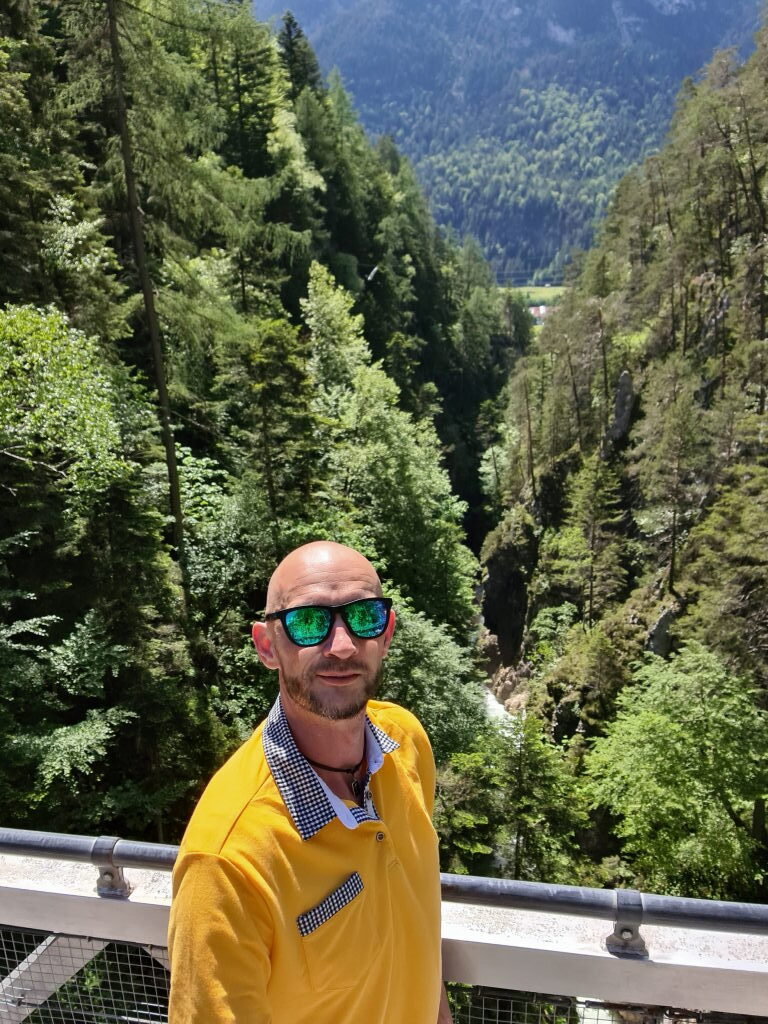 Sebastian mit Sonnenbrille und gelbem Pulli auf der Brücke über die Geisterklamm, dahinter bewaldete Schlucht