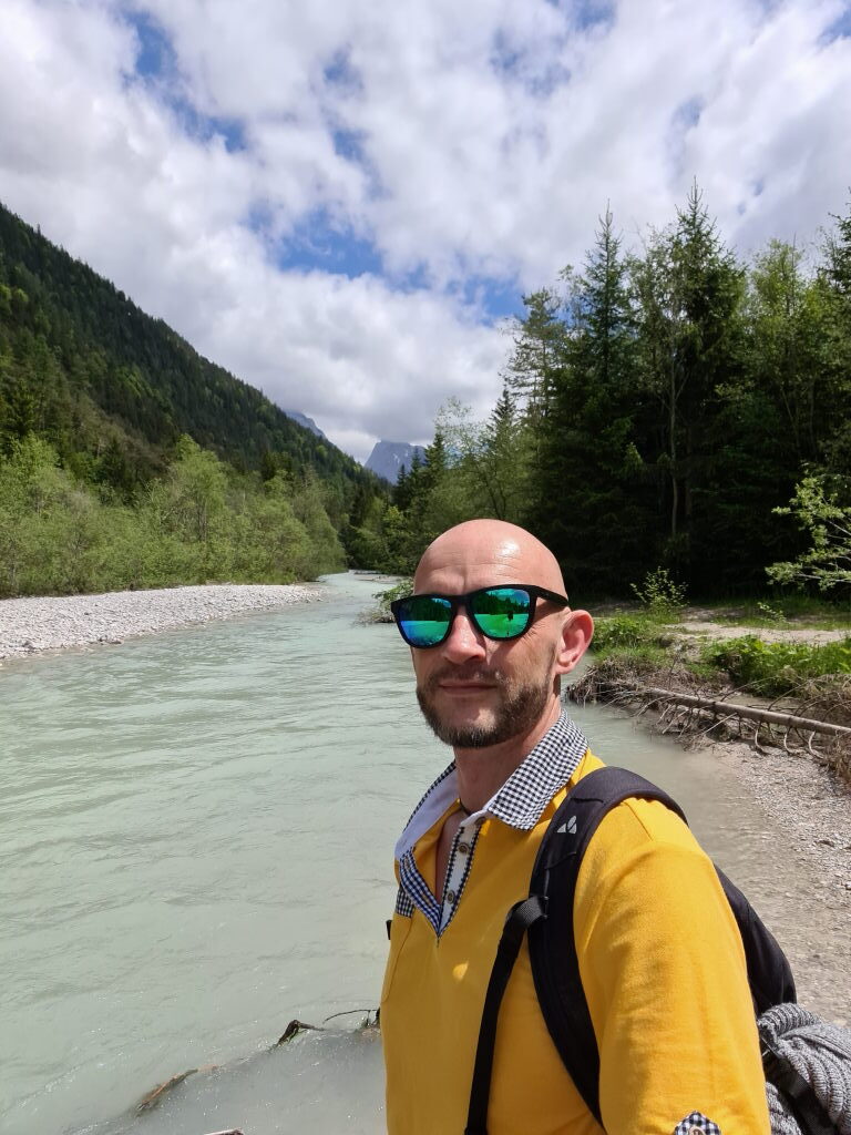 Sebastian mit Sonnenbrille und gelbem Pulli an der türkisen Isar nahe Mittenwald