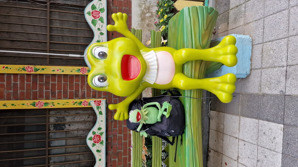 Kermit neben großer Frosch-Skulptur auf Bank Märchendorf Incheon