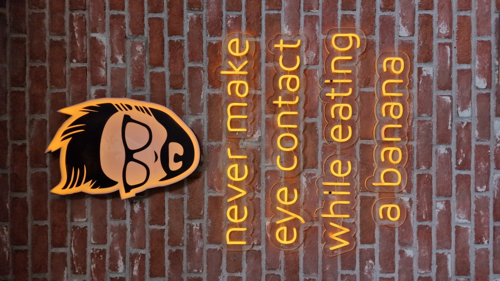 Neonschrift an einer Backsteinwand: never make eye contact while eating a banana
