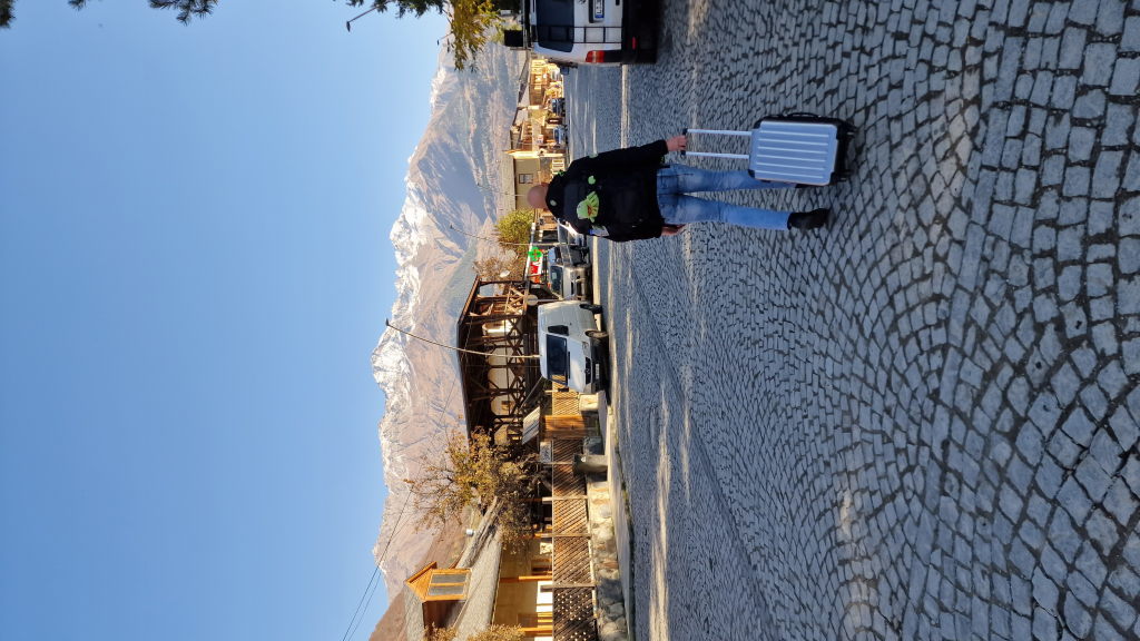 Rückenansicht: Mann mit Koffer auf Kopfsteinpflaster in Mestia, Berge vorne