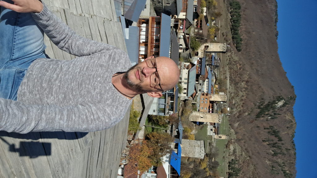 Walter sitzt auf dem Dach eines Svan-Wehrturms mit Mestia-Panorama dahinter