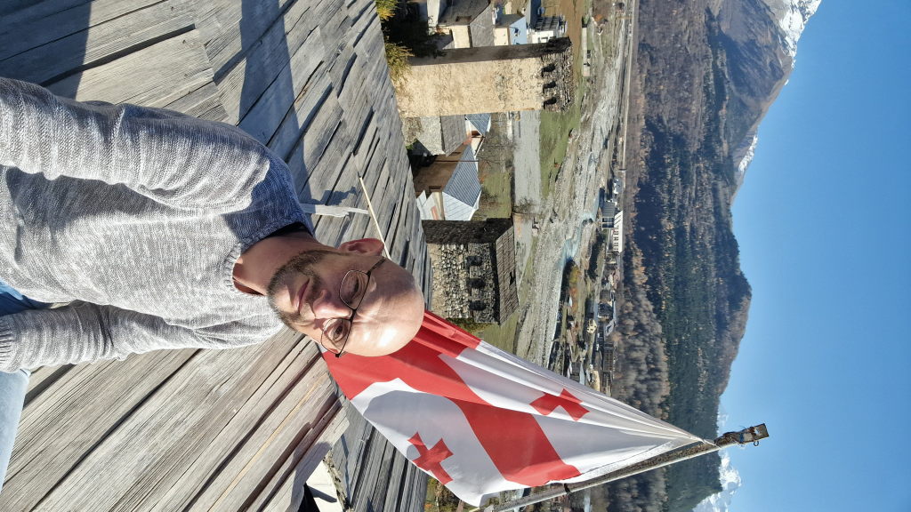 Walter auf Turmdach mit georgischer Flagge, Mestia-Tal im Hintergrund