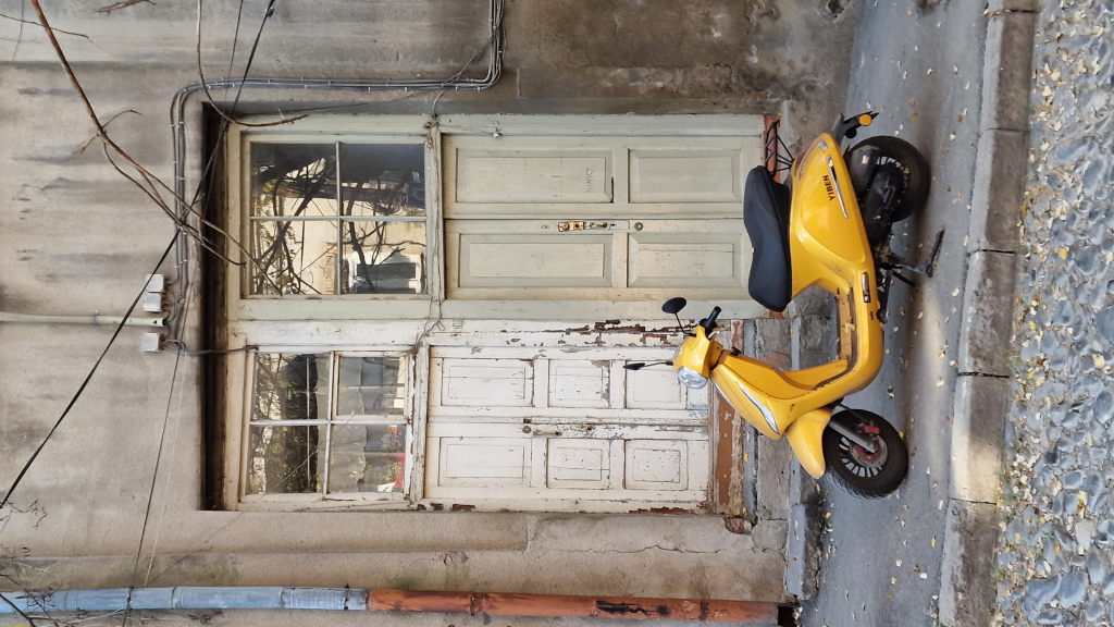 Gelber Motorroller vor alter weißer abblätternder Tür in Tiflis