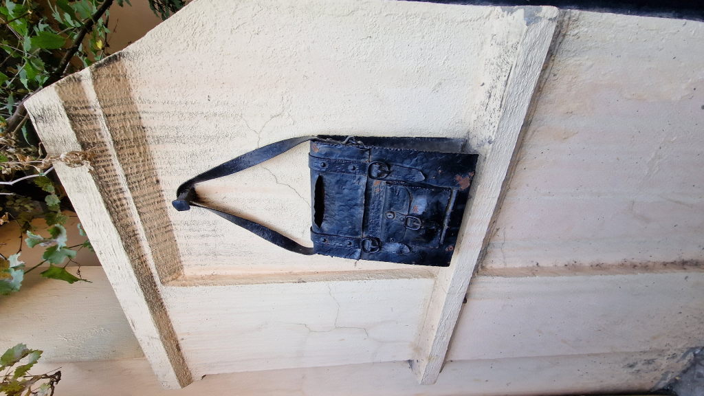 Eiserner Briefkasten als Kunstobjekt in Form einer alten Ledertasche an weißer Wand