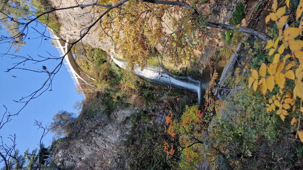 Wasserfall in der Leghvtakhevi-Schlucht in Tiflis mit weißer Bogenbrücke und Herbstlaub