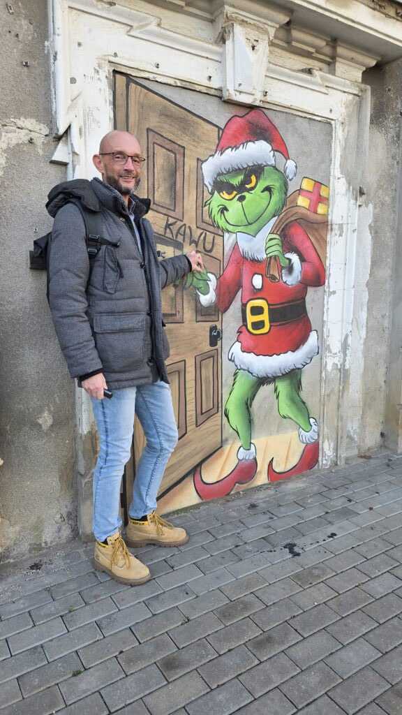 Sebastian Walter neben einem Street-Art-Mural des Grinch als Weihnachtsmann auf einer Eingangstür in Posen